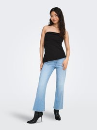 Musta hihaton yläosa, jossa on kerätty rakenne, yhdistetty vaaleansinisiin levenevillä lahkeilla varustettuihin farkkuihin ja mustiin korollisiin nilkkureihin. Sileä kangas ja istuva malli.