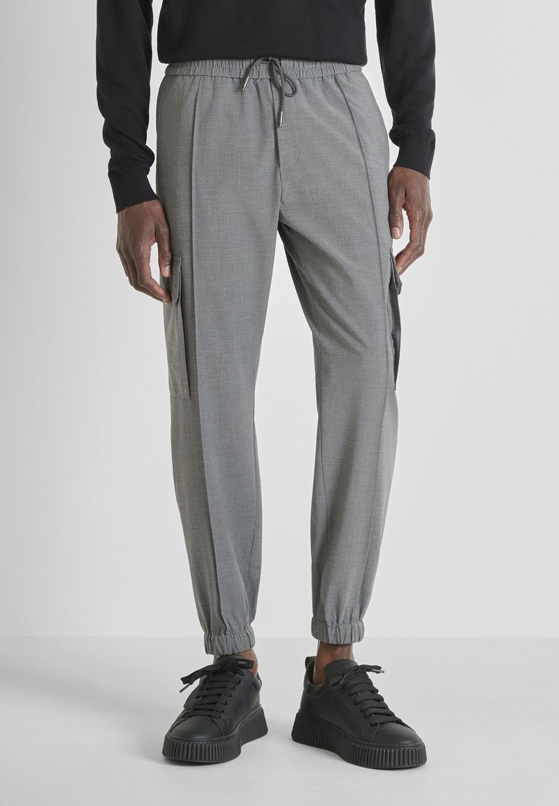 Grijze taps toelopende broek met elastische boorden en een trekkoord in de taille. Voorzien van zijvakjes en een gladde, lichte stof. GCombineerd met zwarte sneakers.