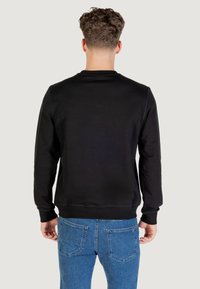 Felpa nera con scollo rotondo e maniche lunghe, caratterizzata da dettagli di cucitura visibili. Abbinata a jeans di denim blu.