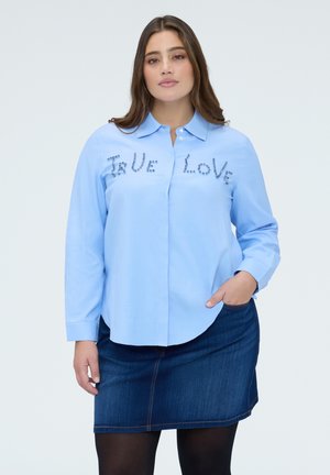 Lichtblauw overhemd met lange mouwen en kraag, versierd met de tekst "TRUE LOVE" in sierstenen, gedragen met een donkere denim rok.