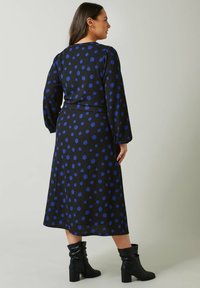 Musta midi-mekko sinisillä pilkuilla, pitkät hihat ja tiukka vyötärö. Yhdistetty polvipitkisiin mustiin löysiin saappaisiin, joissa on teksturoitu kuvio.