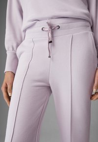 Ljuslila sweatpants i mjukt tyg, med resår och dragsko i midjan samt strukturerad rosa knytning och strömlinjeformade sömmar på sidorna.