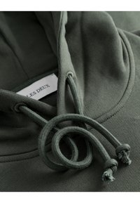 Olivgrön hoodie med snörningar. Har en mjuk textur, en känguruficka och en liten etikett med "LES DEUX" inuti halsen.
