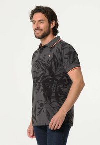 Grijze poloshirt met zwarte bladenprint, contrasterende oranje kraag en mouwen, gemaakt van zachte stof, geschikt voor casual gelegenheid.