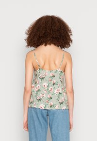 Débardeur floral en tissu vert, avec des bretelles fines et une coupe décontractée. Le design comprend des fleurs roses et des feuilles vertes. Texture lisse.