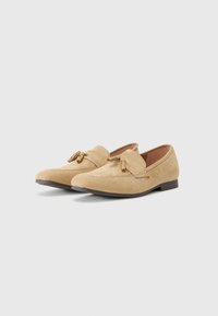 Beige Wildlederloafer mit runder Zehenpartie, dekorativem Oberband und Schnürung, flachem Absatz und gesteppten Akzenten entlang der Kanten.