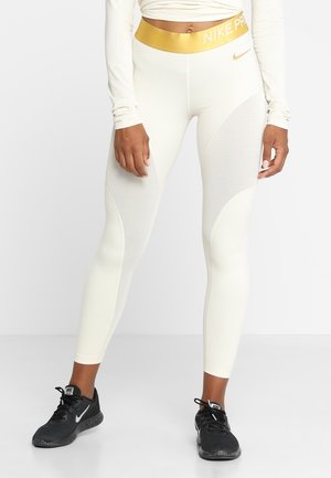 Leggings blancos con una textura acanalada, que presentan una cinturilla de rayas doradas etiquetada como "NIKE PRO" y acentos lisos en los lados.