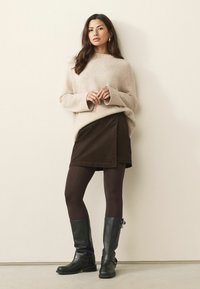 Beige wool sweater, brown wrap skirt, brown tights, and black knee-high leather boots with metallic accents.