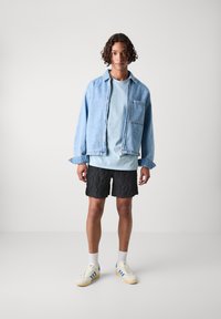 Denim jakna svijetloplave boje, kratki rukavi svijetloplena majica ispod, crne teksturirane kratke hlače i kremaste tenisice s plavim prugama.