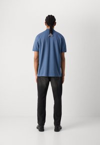 Tricou albastru cu mânecă scurtă, cu croială dreaptă, asortat cu blugi negri cu croială dreaptă și pantofi negri. Material neted, fără modele vizibile.