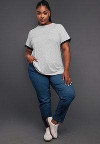 Harmaa t-paita mustalla pitsireunuksella hihoissa, yhdistettynä sinisiin jeansseihin ja valkoisiin lenkkareihin. Paidassa on rento leikkaus ja sivutasku.