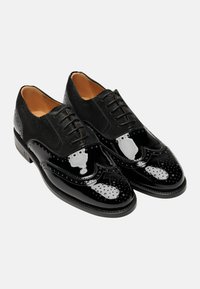 Schwarze Lederbrogues mit einer Kombination aus glänzenden und Wildleder-Oberflächen, detaillierten Perforationen und einem Schnürdesign in klassischer Silhouette.