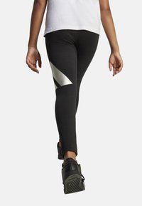 Leggings negros con un acento diagonal metálico plateado, hechos de material elástico, con una silueta ajustada y longitud hasta el tobillo.