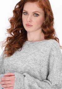 Maglione grigio chiaro, testurizzato, con scollatura ampia e polsini a costine. Il materiale morbido cade delicatamente sulle spalle e sulle braccia.