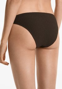 Fekete bikini alsó, texturált anyaggal, magas szabású lábakkal és széles derékpánttal, oldalról és hátulról nézve.