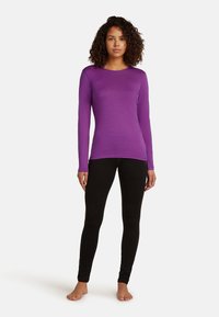 Lila långärmad topp med rund halsringning, parat med svarta leggings. Tyget ser slätt och åtsittande ut, designat för komfort.