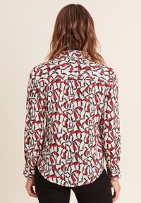 Camicia a maniche lunghe con una base bianca e un motivo geometrico in nero, rosso e blu navy. Tessuto testurizzato con orlo curvo e polsini con bottoni.