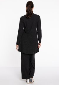 Dunkelgraues langes Tunika mit seitlichen Schlitzen und passenden weiten Hosen, gefertigt aus einem weichen Stoff, kombiniert mit silbernen, hohen Stiefeletten.