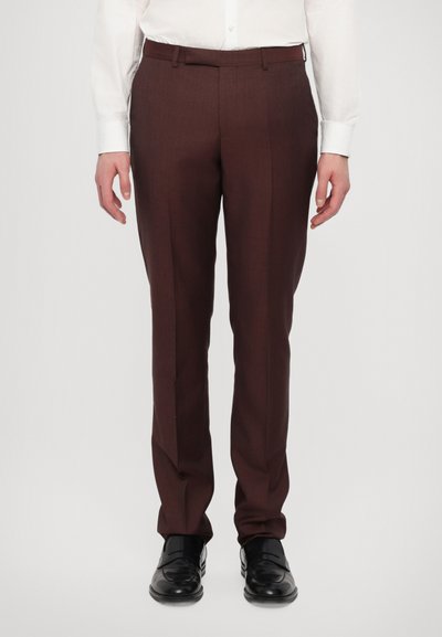 Pantalon marron ajusté avec une texture lisse et une coupe slim, associé à une chemise blanche à boutons et des chaussures en cuir noires.