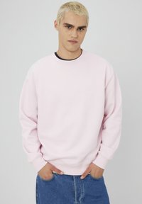 Sweat-shirt en coton rose avec un col rond et des manches longues, comportant des poignets et un ourlet côtelés, ainsi qu'un petit logo blanc sur le devant.
