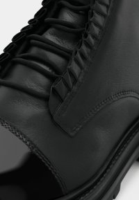 Schwarze Lederknöchelstiefelette mit strukturiertem Obermaterial und einzigartigen Rüschendetails, flacher Gummiuntersohle und sichtbaren Nähakzenten.