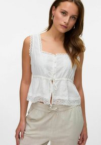 Haut blanc avec des bordures en dentelle, décolleté carré, boutons à l'avant et détail à nouer. Tissu léger, coupe décontractée et motif texturé.