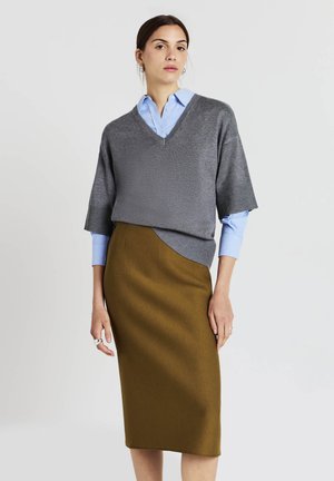 Maglione grigio lavorato a maglia con scollo a V e maniche corte indossato sopra una camicia azzurra con bottoni. Gonna midi aderente verde oliva con una texture liscia.