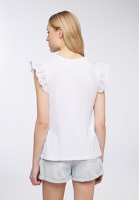 T-shirt bianco in cotone con maniche a volant in broderie anglaise, scollo rotondo, vestibilità comoda, abbinato a pantaloni shorts in denim chiaro.