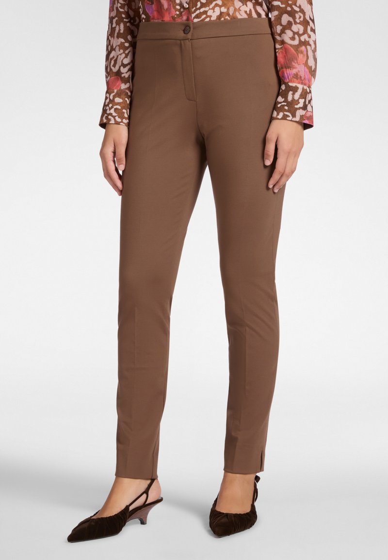 Pantaloni marroni su misura con una texture liscia, vestibilità slim e chiusura con bottone frontale. Spacchetti all'orlo alla caviglia. Abbinati a tacchi in velluto scuro.