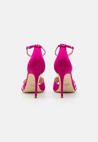 Sandali con tacco alto in satin fucsia con cinturino alla caviglia, con dettagli argentati e design open toe. Tacchi a stiletto e texture liscia.