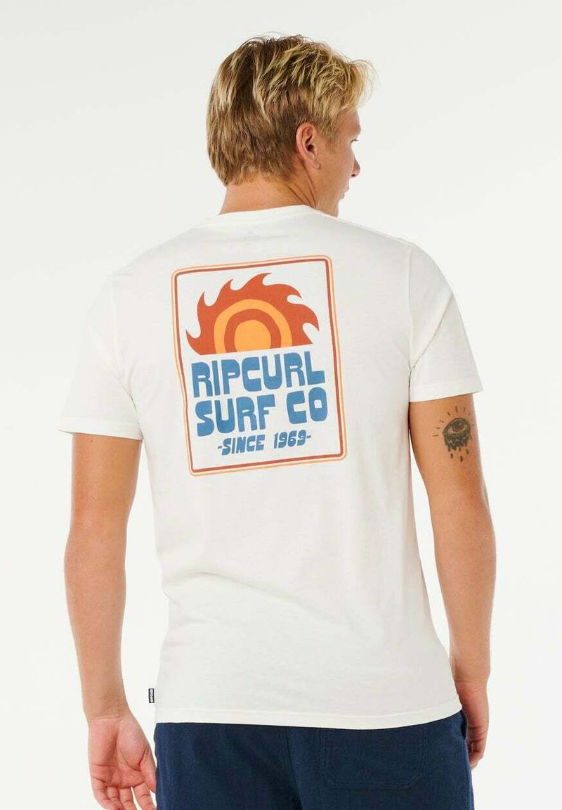 T-shirt en coton blanc avec un motif graphique coloré au dos, représentant un soleil et le texte "RIPCURL SURF CO - DEPUIS 1969".