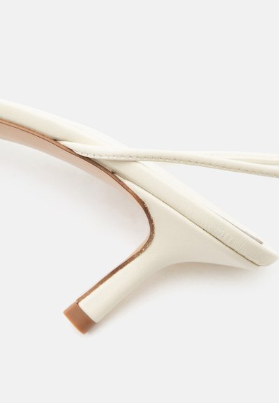 Λευκά δερμάτινα slingback kitten heels με λεπτό λουράκι και καφέ άκρο στη φτέρνα, εμφανιζόμενα από πλάγια γωνία σε λευκό φόντο.