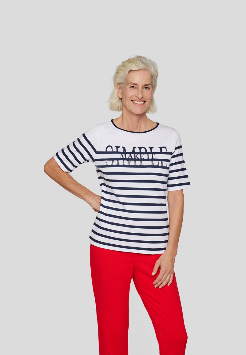 White t-shirt with navy horizontal stripes featuring the word "SIMPLE" printed across the front, paired with red trousers. Short sleeves.