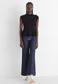 Black peplum top with a high neckline paired with high-waisted, wide-leg dark denim jeans and white sneakers with a gum sole.