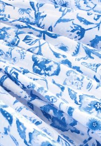 Blaues stoff mit floralen Mustern auf weißem Hintergrund, das komplizierte Motive zeigt, eine weiche Textur hat und sanfte Falten im Material aufweist.