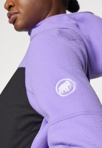Fleece hoodie in lavender and black, featuring a round white logo of an elephant on the arm, showcasing a smooth texture and sporty design.