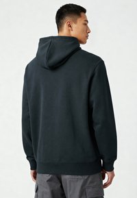 Donkergroene hoodie van een zachte, gestructureerde stof, met een kangoeroezak en een capuchon met trekkoord. Ribgebreide boorden en zoom maken het ontwerp compleet.