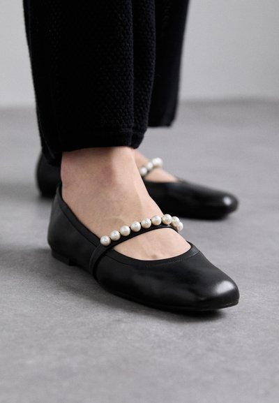 Black leather ballet flats featuring a round toe and decorative faux pearl detailing along the strap. Smooth texture with a low heel.
