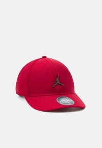 Rote Kappe aus Stoff mit strukturiertem Design, das ein schwarzes Jumpman-Logo und einen flachen Schirm aufweist. Enthält ein rundes Etikett auf dem Visier.
