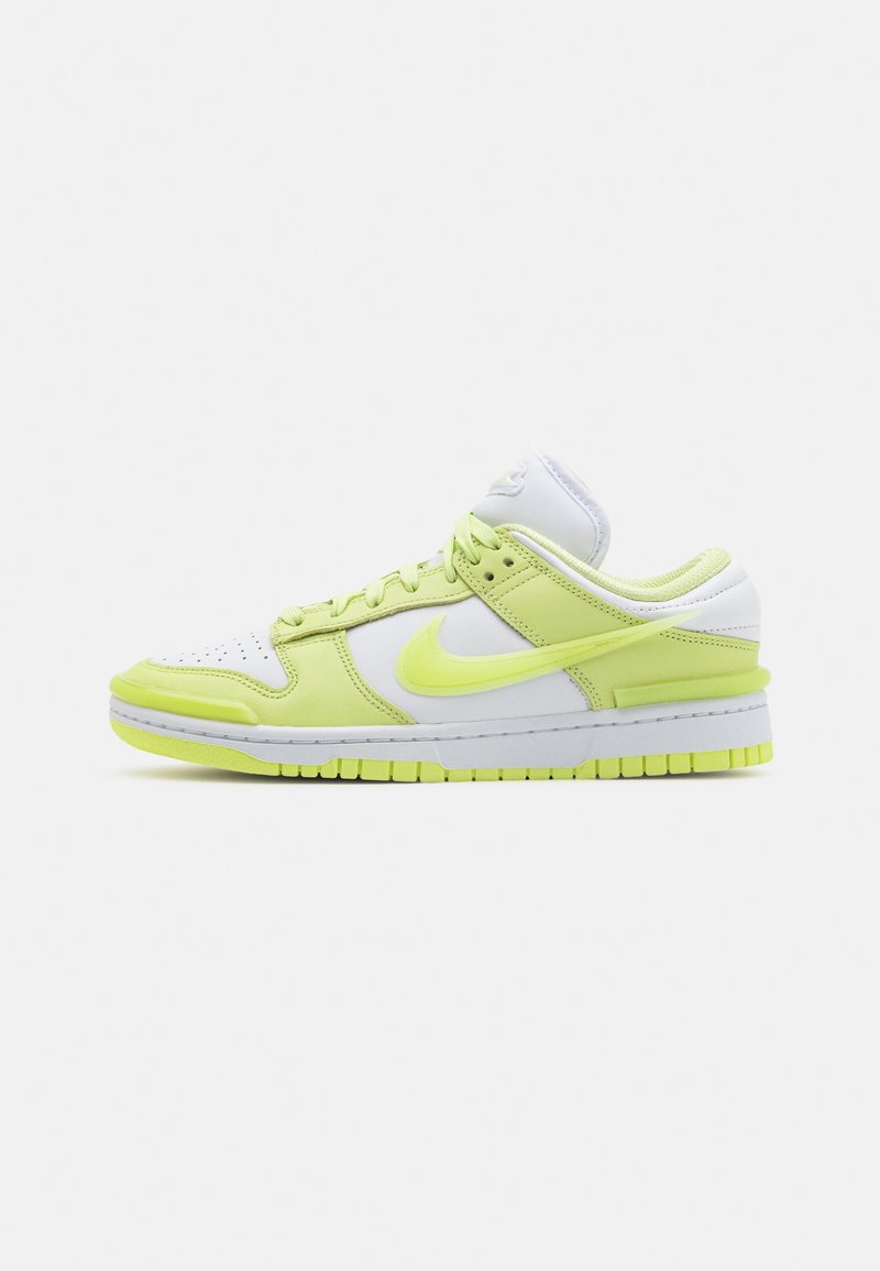 Basket basse Nike avec base blanche et surpiqûres jaune fluo, lacets et semelle, présentée de profil sur un fond clair uni.