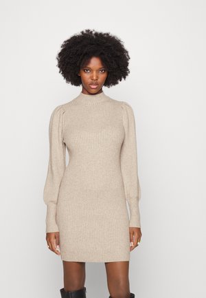 Robe pull beige à côtes avec un col haut et des manches longues bouffantes, présentant une silhouette ajustée et un tissu texturé.