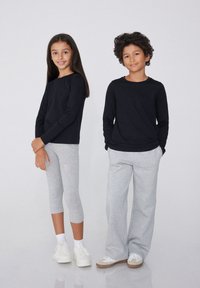 Dva děti stojí vedle sebe. Jedno má na sobě černé tričko s dlouhým rukávem a šedé legíny, druhé má černé tričko s dlouhým rukávem a šedé tepláky.