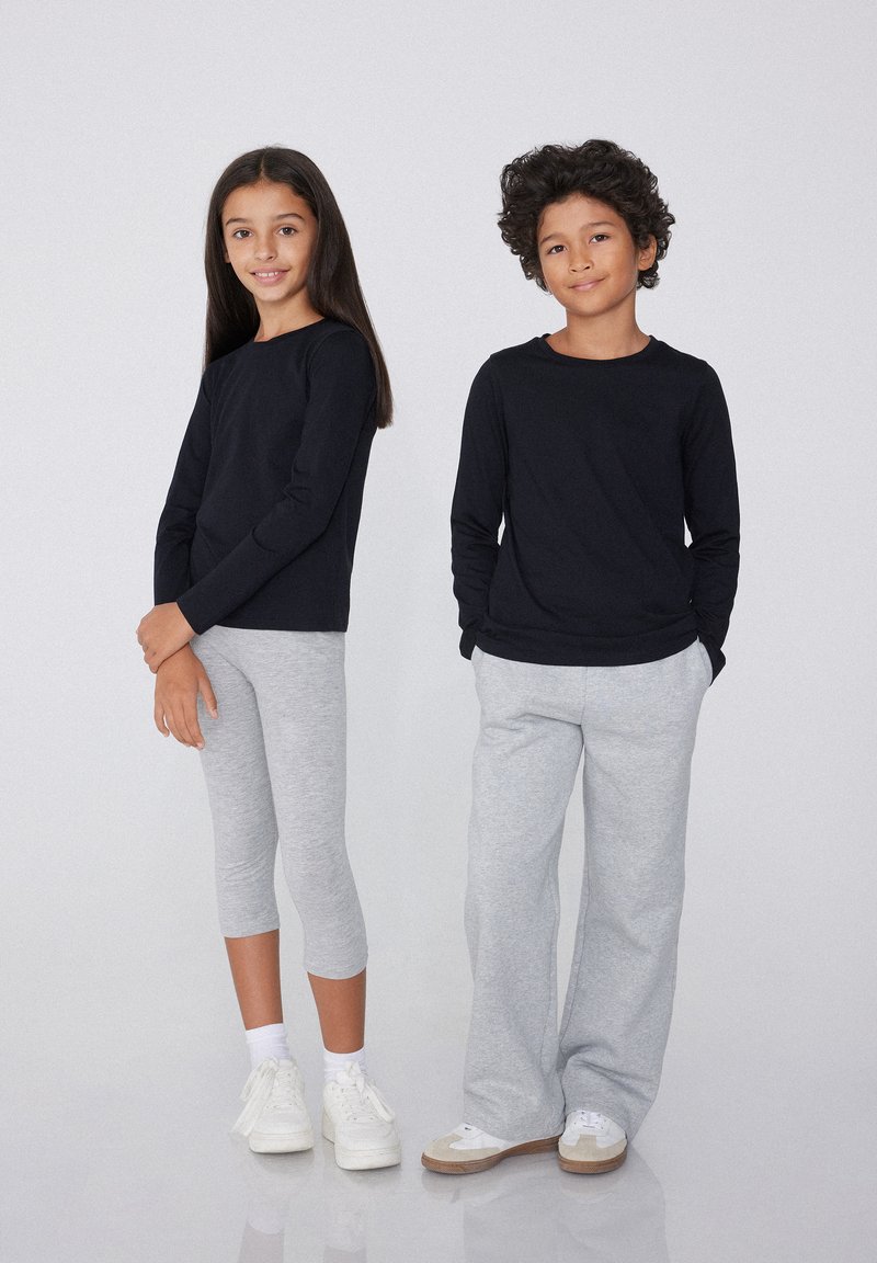 Dva děti stojí vedle sebe. Jedno má na sobě černé tričko s dlouhým rukávem a šedé legíny, druhé má černé tričko s dlouhým rukávem a šedé tepláky.