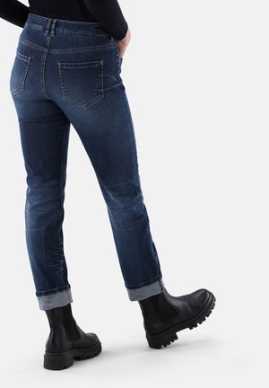 Dunkelblaue, eng anliegende Jeans mit umgeschlagenen Bündchen, fünf Taschen und dezentem Ausbleichen. Kombiniert mit schwarzen Stiefeletten mit dicken Sohlen.