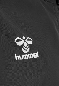 Svart tyg med en vit logotyp med ett bi och geometriska mönster, som är tydligt placerad i den nedre delen av bilden.