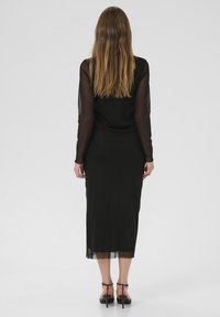 Black dress with long sheer sleeves, fitted silhouette, and mid-calf length. Features transparent paneling at the hem and simple design.