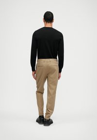 Juodas ilgomis rankovėmis marškinėliai, tan spalvos kelnės su dviem užpakaliniais kišenėmis ir juodi batai. Lygus audinys ir prigludęs dizainas su šiuolaikine siluetu.