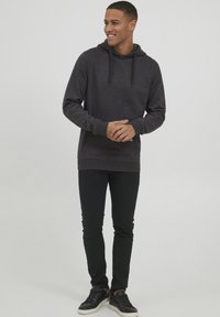 Dark gray hoodie with a drawstring, featuring a kangaroo pocket, paired with black slim-fit pants and black sneakers with white soles.