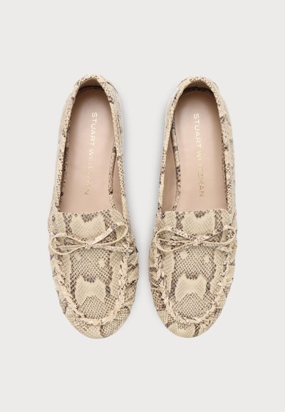 Paire de mocassins beiges à motif peau de serpent, avec bords tressés et nœuds à l’avant, vus de dessus sur un fond clair.