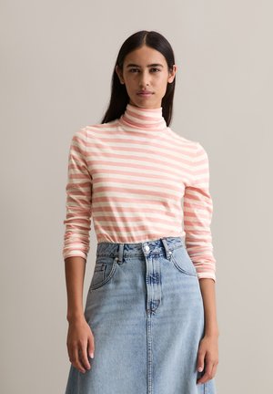 Maglione a collo alto a righe rosa chiaro e bianco, abbinato a una gonna di jeans blu a vita alta con chiusura a bottoni e tasche laterali.